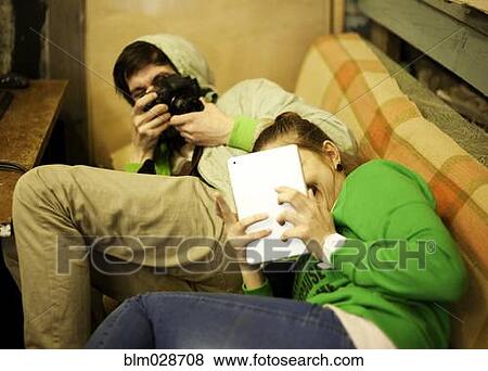 Caucasian man photographing girlfriend on sofa View Large Photo Image Stock Photo - Caucasian man photographing girlfriend on sofa. Fotosearch