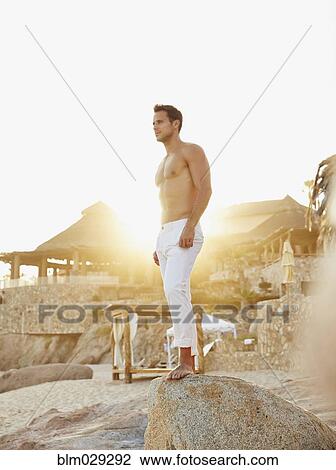 Stock Image - Caucasian man standing on rock at beach. Fotosearch