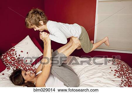 Picture - Caucasian mother and son playing on bed. Fotosearch