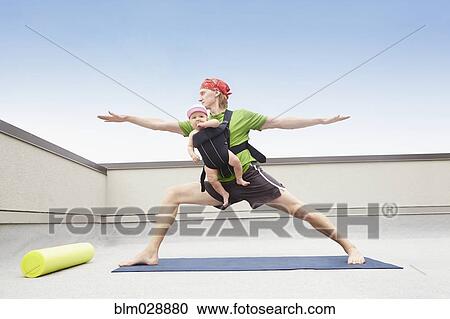 Stock Image - Father practicing yoga and holding baby. Fotosearch