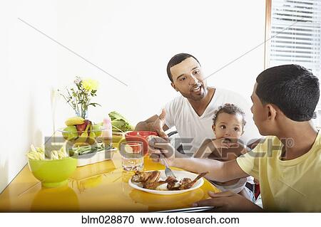 Stock Image - Hispanic father and children eating together. Fotosearch