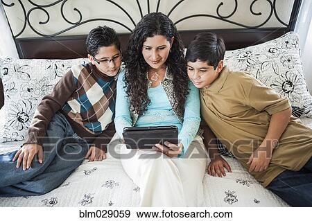 Hispanic mother reading to sons on bed View Large Photo Image Stock Photo - Hispanic mother reading to sons on bed. Fotosearch