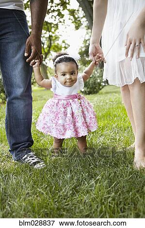 Stock Photo - Parents helping daughter walk in park. Fotosearch