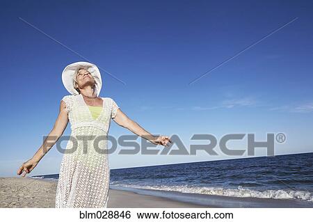 Stock Photograph - Senior woman standing on tropical beach. Fotosearch
