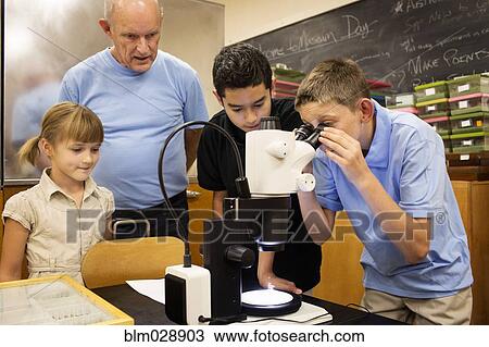 Stock Image - Teacher and students using microscope in laboratory. Fotosearch
