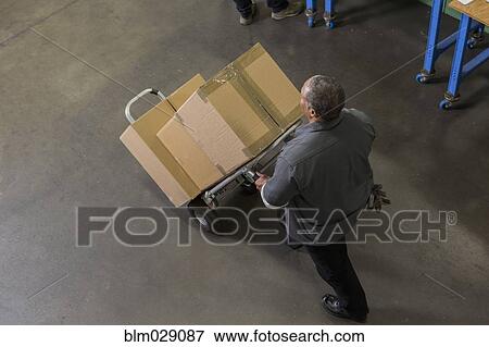 Worker carting boxes on hand truck in warehouse View Large Photo Image Stock Photo - Worker carting boxes on hand truck in warehouse. Fotosearch