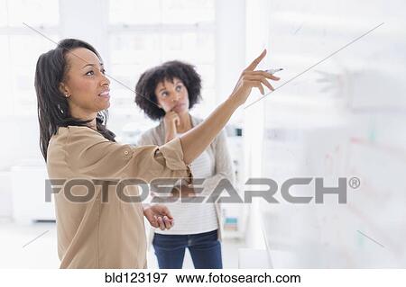 Stock Photo - African American businesswomen at whiteboard in office. Fotosearch
