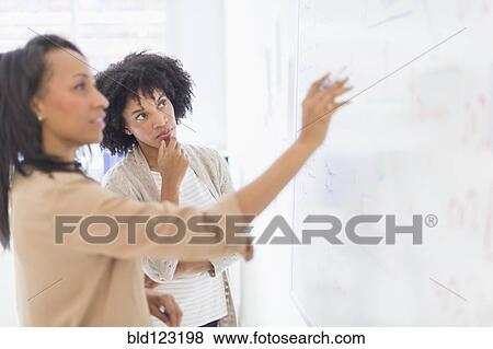 Stock Photo - African American businesswomen at whiteboard in office. Fotosearch