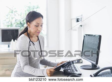 Stock Image - African American doctor looking down at clipboard. Fotosearch