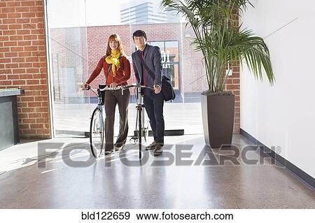 Business people wheeling bicycles in office View Large Photo Image Stock Photo - Business people wheeling bicycles in office. Fotosearch