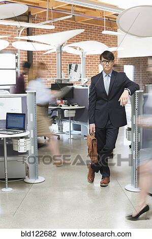 Stock Image - Businessman standing in busy office. Fotosearch