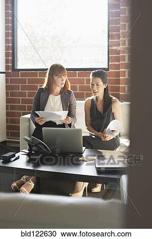 Stock Image - Businesswomen working together in office. Fotosearch