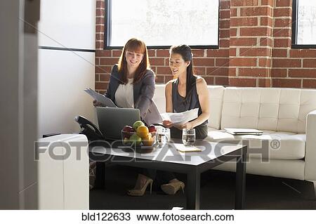 Stock Image - Businesswomen working together in office. Fotosearch