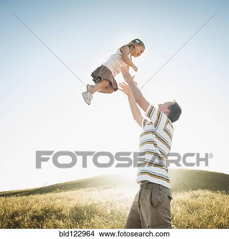 Picture - Caucasian father lifting daughter overhead in rural field. Fotosearch