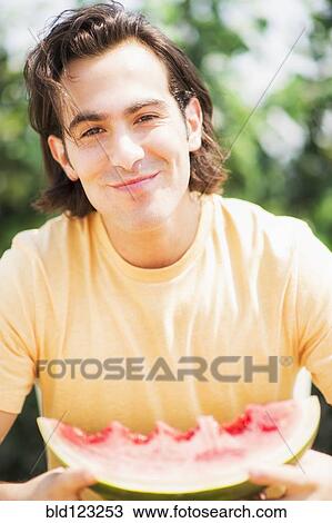 Stock Image - Caucasian man eating watermelon outdoors. Fotosearch