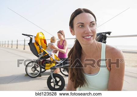 Stock Photo - Caucasian mothers with strollers on beach boardwalk. Fotosearch
