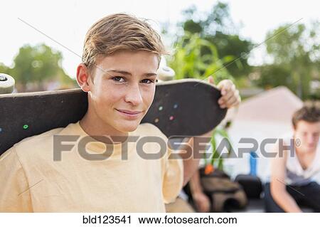 Stock Image - Caucasian teenage boy holding skateboard. Fotosearch