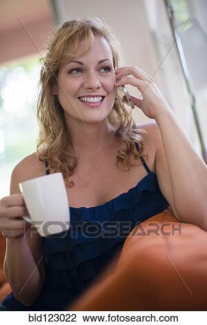 Stock Image - Caucasian woman drinking coffee and talking on cell phone. Fotosearch