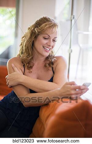 Stock Image - Caucasian woman using cell phone on sofa. Fotosearch