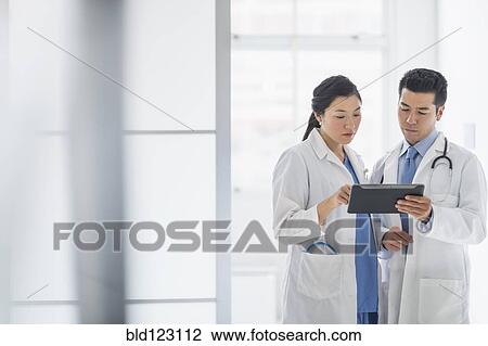 Doctors using digital tablet in hospital corridor View Large Photo Image Stock Image - Doctors using digital tablet in hospital corridor. Fotosearch