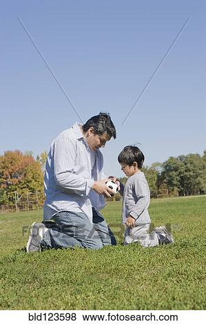 Stock Photo - Hispanic father and son playing soccer outdoors. Fotosearch