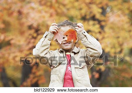 Stock Photo - Hispanic girl holding autumn leaves over her eyes. Fotosearch