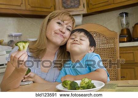 Stock Image - Hispanic mother and son eating broccoli. Fotosearch