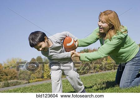 Picture - Hispanic mother and son playing football outdoors. Fotosearch