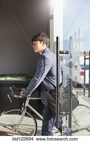Korean businessman wheeling bicycle in office View Large Photo Image Picture - Korean businessman wheeling bicycle in office. Fotosearch