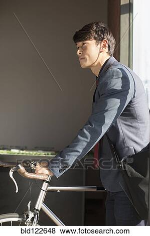 Korean businessman wheeling bicycle in office View Large Photo Image Stock Photo - Korean businessman wheeling bicycle in office. Fotosearch
