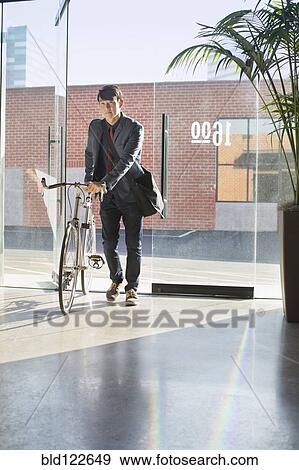 Stock Photo - Korean businessman wheeling bicycle in office. Fotosearch