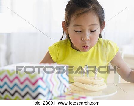 Stock Image - Korean girl blowing out candles on birthday cake. Fotosearch