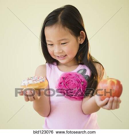 Stock Photograph - Korean girl choosing between apple and donut. Fotosearch