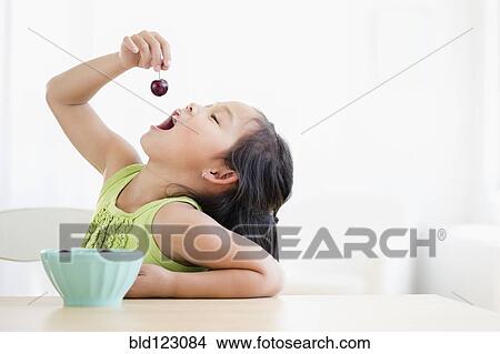 Picture - Korean girl eating bowl of fruit. Fotosearch