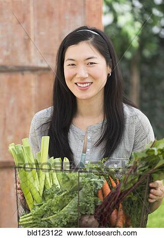 Stock Image - Korean woman carrying basket of vegetables. Fotosearch