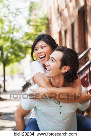 Man carrying girlfriend piggyback on urban sidewalk View Large Photo Image Picture - Man carrying girlfriend piggyback on urban sidewalk. Fotosearch