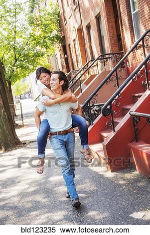 Man carrying girlfriend piggyback on urban sidewalk View Large Photo Image Stock Photography - Man carrying girlfriend piggyback on urban sidewalk. Fotosearch