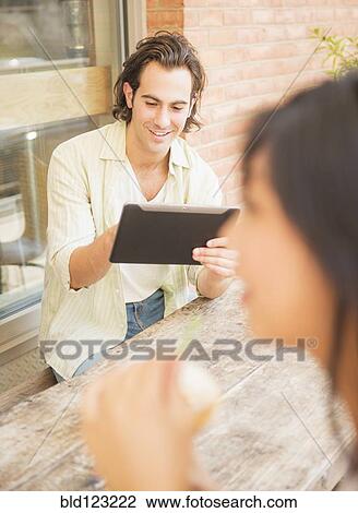 Stock Image - Man using digital tablet at sidewalk cafe. Fotosearch