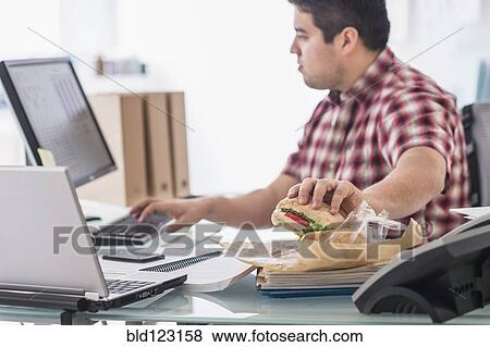 Mixed race businessman eating and working at desk View Large Photo Image Stock Photo - Mixed race businessman eating and working at desk. Fotosearch