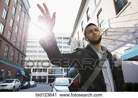 Stock Image - Mixed race businessman hailing taxi on city street. Fotosearch
