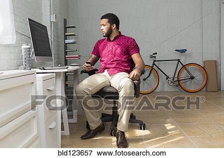 Stock Photo - Mixed race businessman sitting at desk. Fotosearch