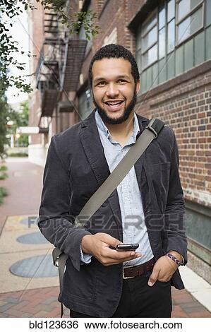 Stock Photograph - Mixed race businessman using cell phone on city sidewalk. Fotosearch