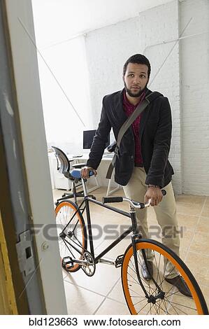 Mixed race businessman wheeling bicycle in office View Large Photo Image Stock Image - Mixed race businessman wheeling bicycle in office. Fotosearch