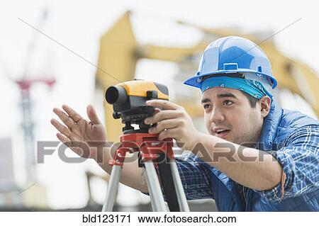 Stock Image - Mixed race engineer using theodolite at construction site. Fotosearch