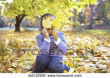 Stock Image - Mixed race girl holding autumn leaves over her eyes. Fotosearch