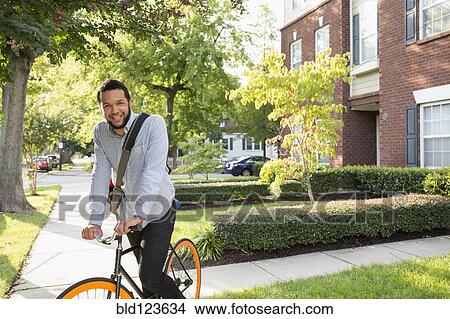 Picture - Mixed race man on bicycle on suburban sidewalk. Fotosearch