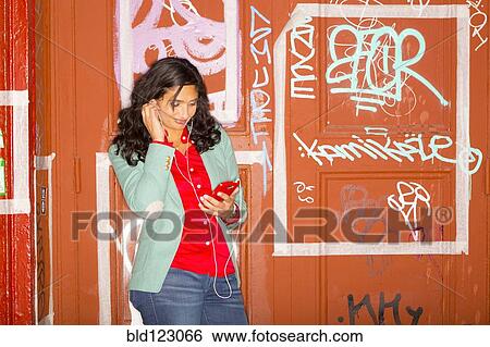 Mixed race woman listening to headphones against graffiti wall View Large Photo Image Stock Photograph - Mixed race woman listening to headphones against graffiti wall. Fotosearch