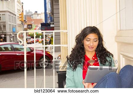 Mixed race woman using digital tablet on urban front stoop View Large Photo Image Picture - Mixed race woman using digital tablet on urban front stoop. Fotosearch