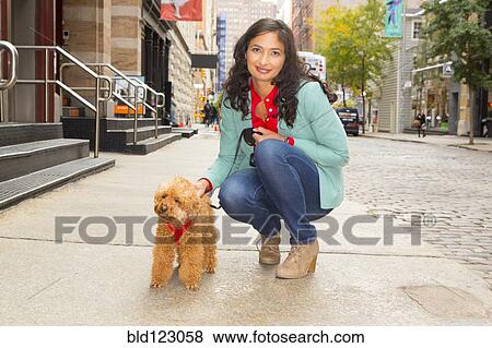 Stock Photo - Mixed race woman walking dog on urban sidewalk. Fotosearch