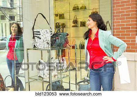 Stock Image - Mixed race woman window shopping at purse shop. Fotosearch